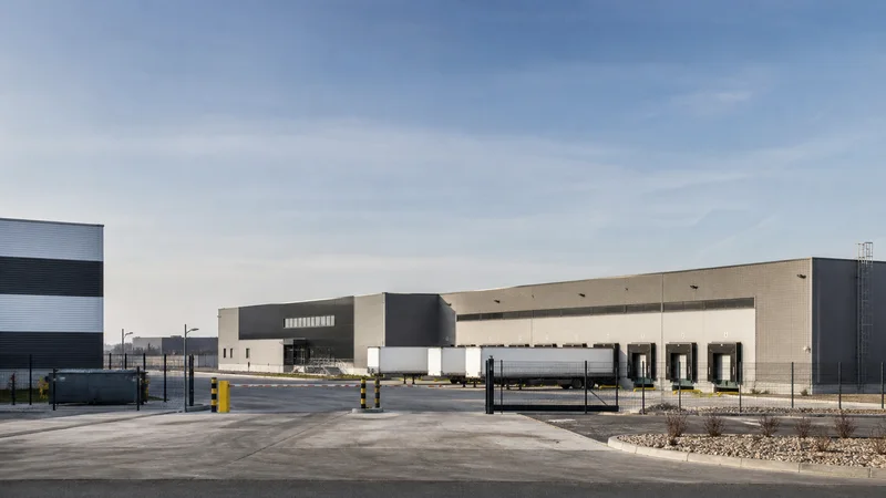 Wide establishing view of a distribution centre and loading yard, soft daylight, clear open sky for overlaid text