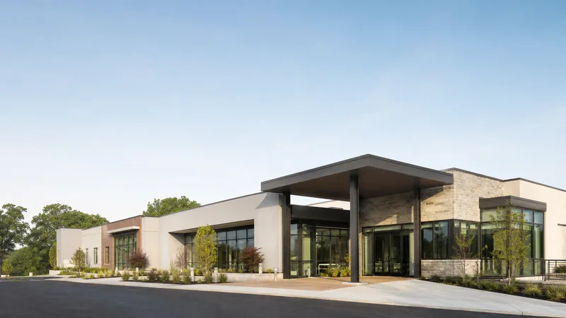 Wide establishing view of a modern medical clinic building, soft daylight, open sky above for overlaid text