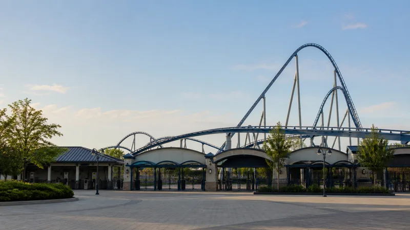 Wide establishing view of a amusement park gates with towering roller coaster, soft daylight, open sky above for overlaid text