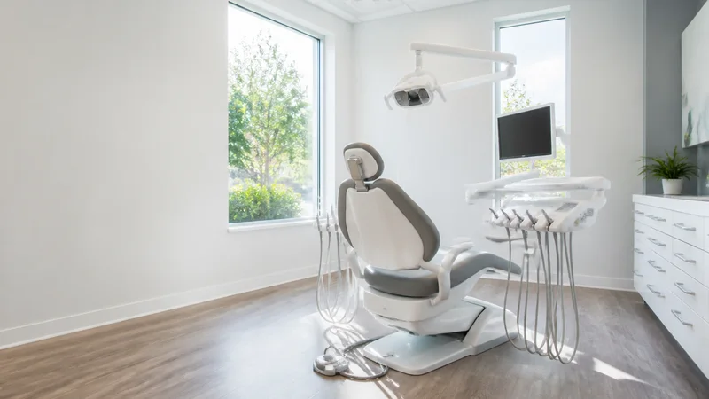 Wide interior view of a clean dental treatment room with no people, bright daylight through the windows, clean uncluttered foreground for text