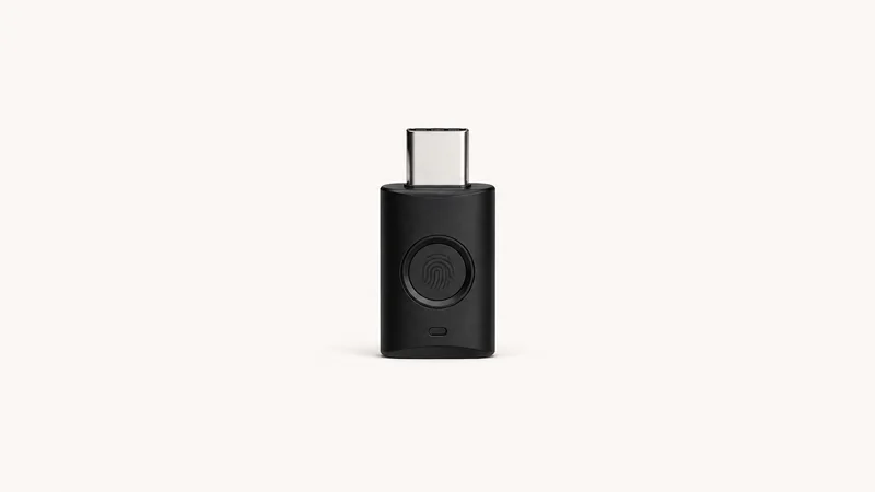 Isolated a USB-C authentication key with a fingerprint sensor centred on a seamless pale off-white studio background, generous empty margin on every side for overlaid branding