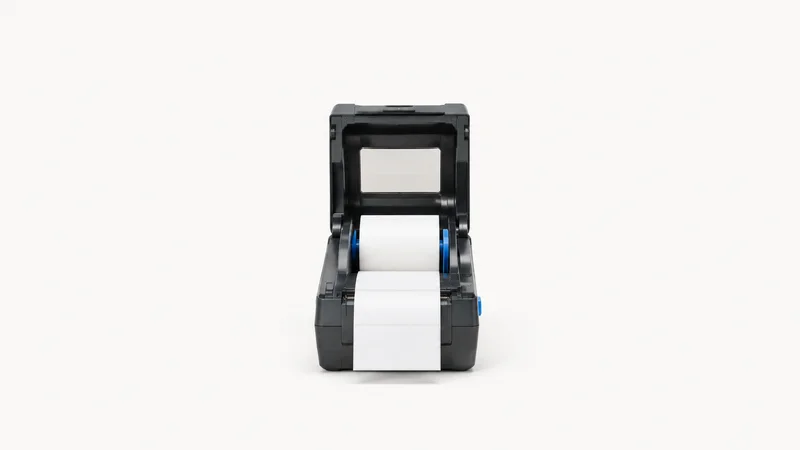 Isolated a thermal label printer with a blank roll loaded centred on a seamless pale off-white studio background, generous empty margin on every side for overlaid branding