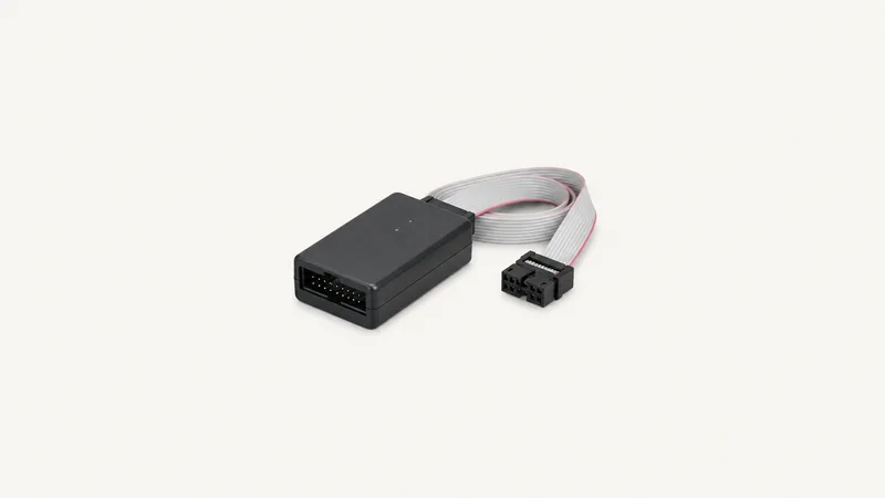 Isolated a hardware debug probe with a ribbon cable centred on a seamless pale off-white studio background, generous empty margin on every side for overlaid branding