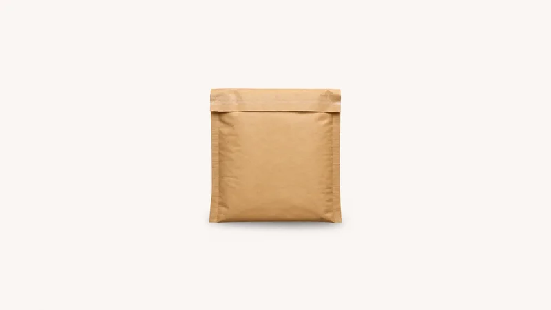 Isolated a kraft-brown padded courier satchel with a tamper-evident seal strip centred on a seamless pale off-white studio background, generous empty margin on every side for overlaid branding