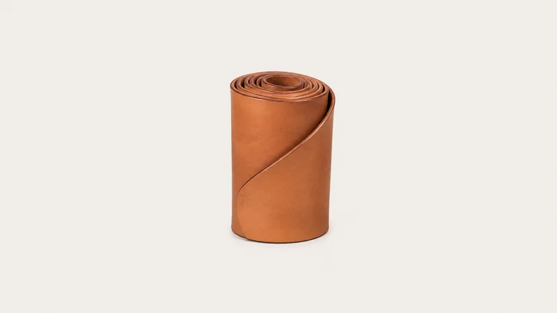 Isolated a rolled shoulder of vegetable-tanned leather with a burnished edge centred on a seamless pale off-white studio background, generous empty margin on every side for overlaid branding