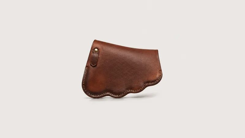 Isolated a hand-stitched leather saddle flap with a scalloped edge centred on a seamless pale off-white studio background, generous empty margin on every side for overlaid branding