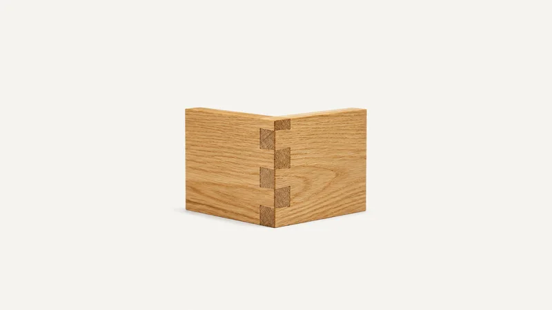 Isolated a hand-cut dovetail joint in oak centred on a seamless pale off-white studio background, generous empty margin on every side for overlaid branding