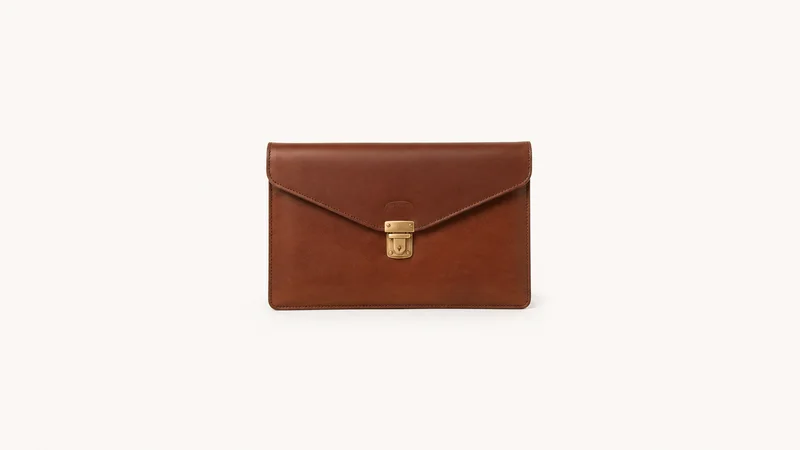 Isolated a leather portfolio case with a brass clasp centred on a seamless pale off-white studio background, generous empty margin on every side for overlaid branding