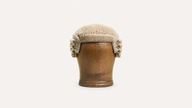 Isolated a barrister's horsehair wig on a wooden head block centred on a seamless pale off-white studio background, generous empty margin on every side for overlaid branding