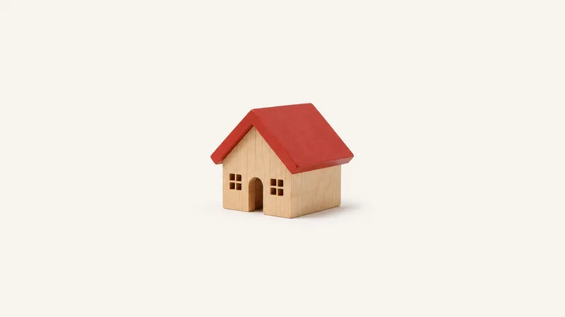Isolated a wooden house-shaped model with a red pitched roof centred on a seamless pale off-white studio background, generous empty margin on every side for overlaid branding