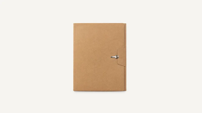 Isolated a blank cardboard candidate folder with a metal fastener centred on a seamless pale off-white studio background, generous empty margin on every side for overlaid branding