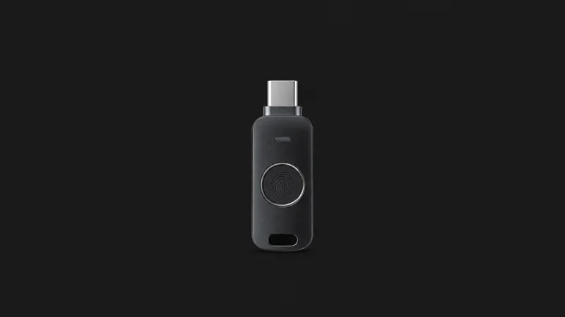 Isolated a USB-C authentication key with a fingerprint sensor centred on a seamless deep charcoal near-black studio background, generous empty margin on every side for overlaid branding