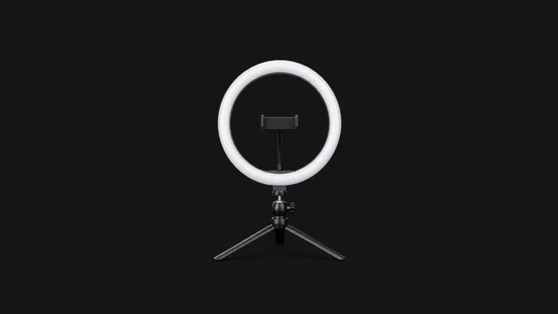 Isolated a ring light on a tabletop tripod centred on a seamless deep charcoal near-black studio background, generous empty margin on every side for overlaid branding