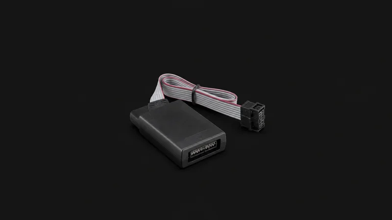 Isolated a hardware debug probe with a ribbon cable centred on a seamless deep charcoal near-black studio background, generous empty margin on every side for overlaid branding