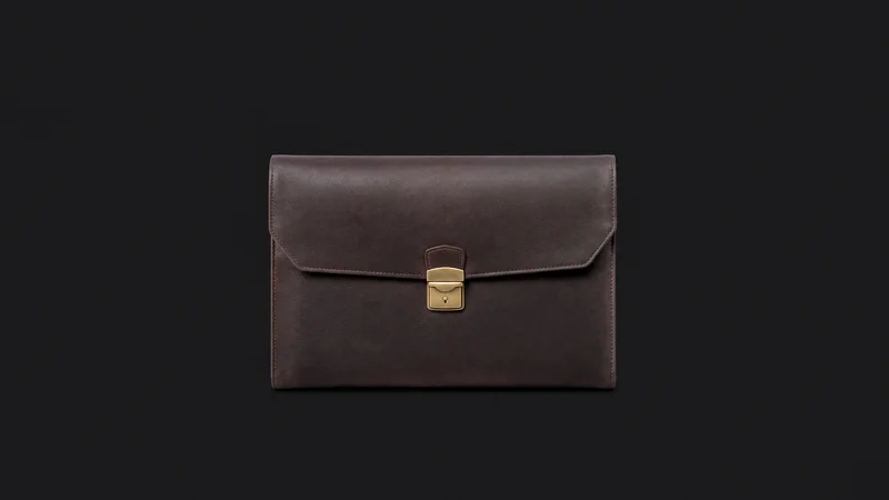 Isolated a leather portfolio case with a brass clasp centred on a seamless deep charcoal near-black studio background, generous empty margin on every side for overlaid branding