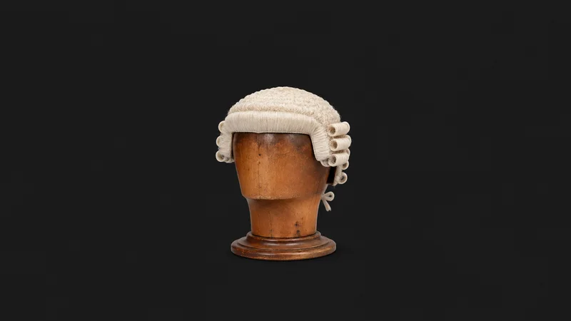 Isolated a barrister's horsehair wig on a wooden head block centred on a seamless deep charcoal near-black studio background, generous empty margin on every side for overlaid branding