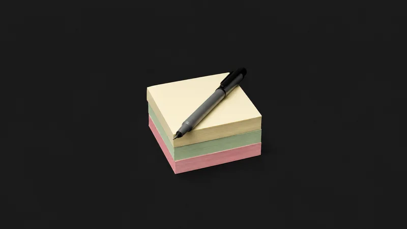 Isolated a stack of blank sticky notes in three colours with a fine marker centred on a seamless deep charcoal near-black studio background, generous empty margin on every side for overlaid branding