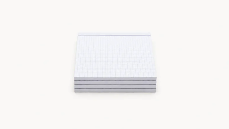 Isolated a stack of blank graph-paper pads centred on a seamless pale off-white studio background, generous empty margin on every side for overlaid branding