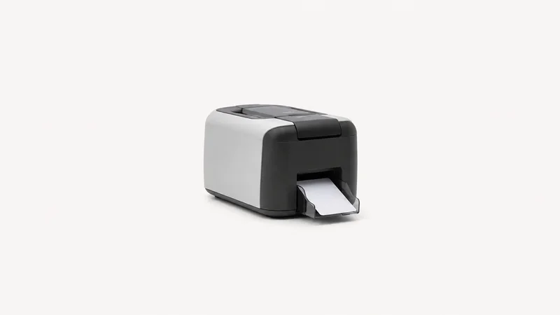 Isolated a desktop id-card printer with a blank card in its output tray centred on a seamless pale off-white studio background, generous empty margin on every side for overlaid branding