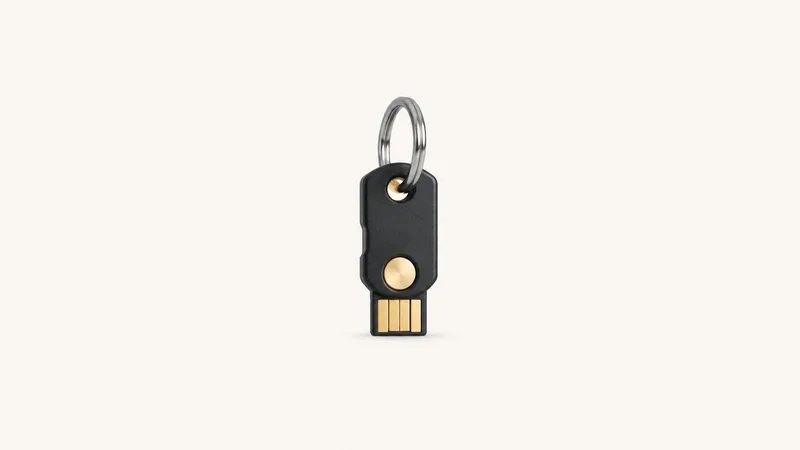 Isolated a hardware security key on a short steel keyring centred on a seamless pale off-white studio background, generous empty margin on every side for overlaid branding