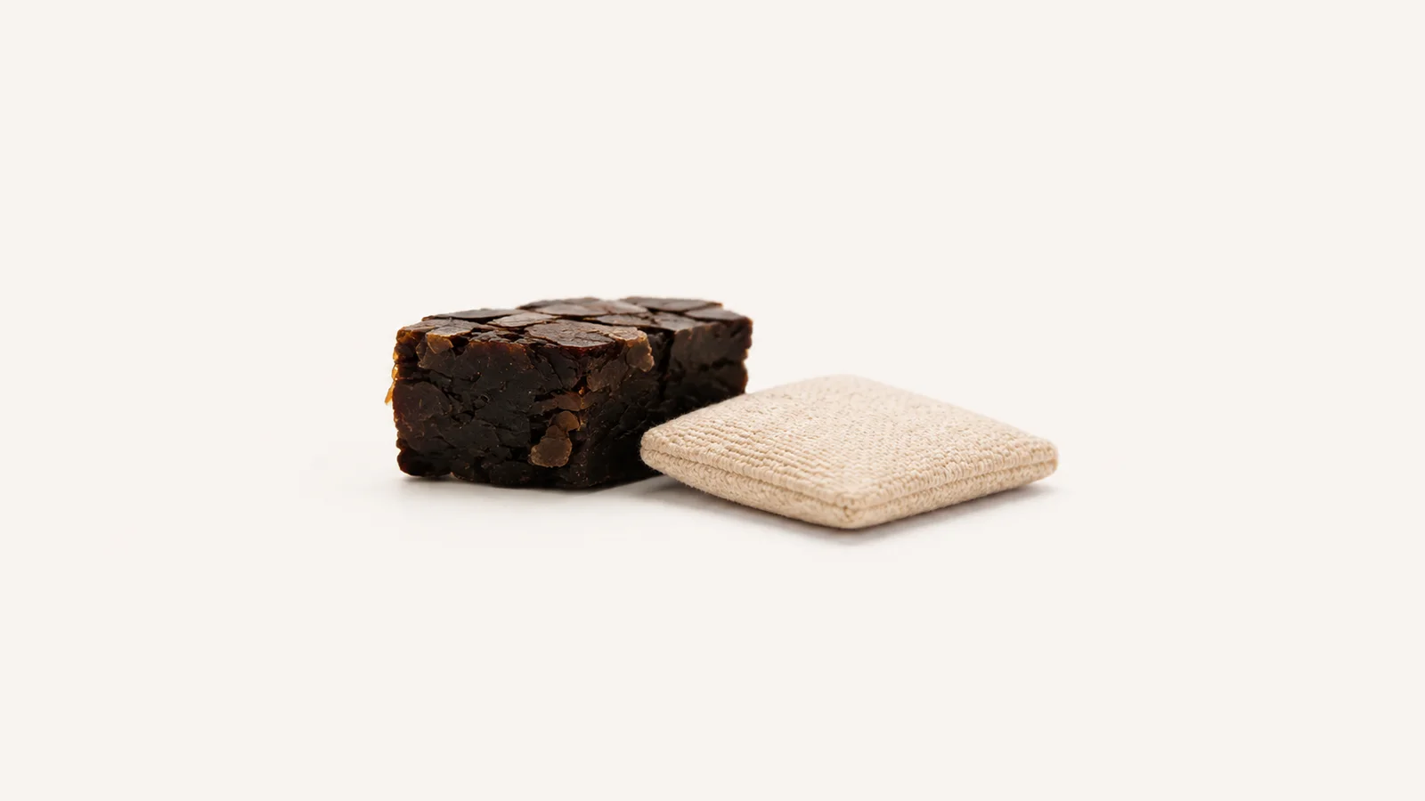 Isolated a block of dark shellac flakes beside a rubbing pad centred on a seamless pale off-white studio background, generous empty margin on every side for overlaid branding