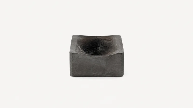 Isolated a graphite shaping block with a scorched hollow centred on a seamless pale off-white studio background, generous empty margin on every side for overlaid branding