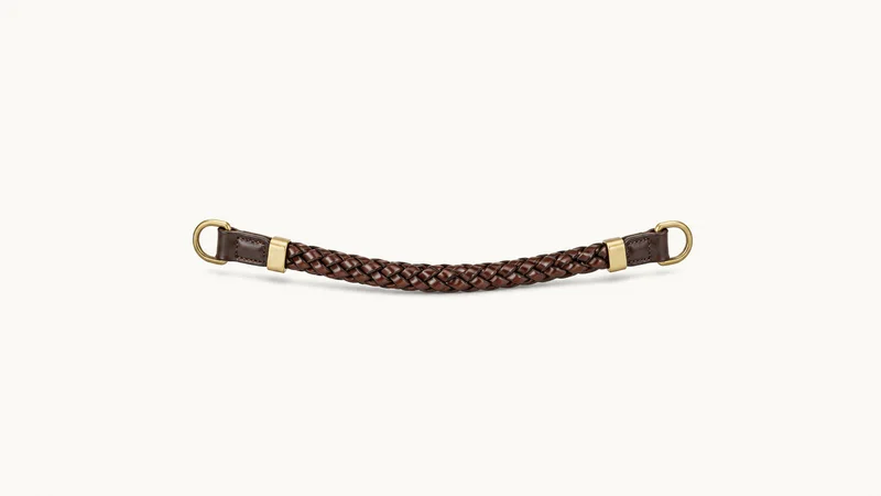 Isolated a plaited leather browband with brass fittings centred on a seamless pale off-white studio background, generous empty margin on every side for overlaid branding