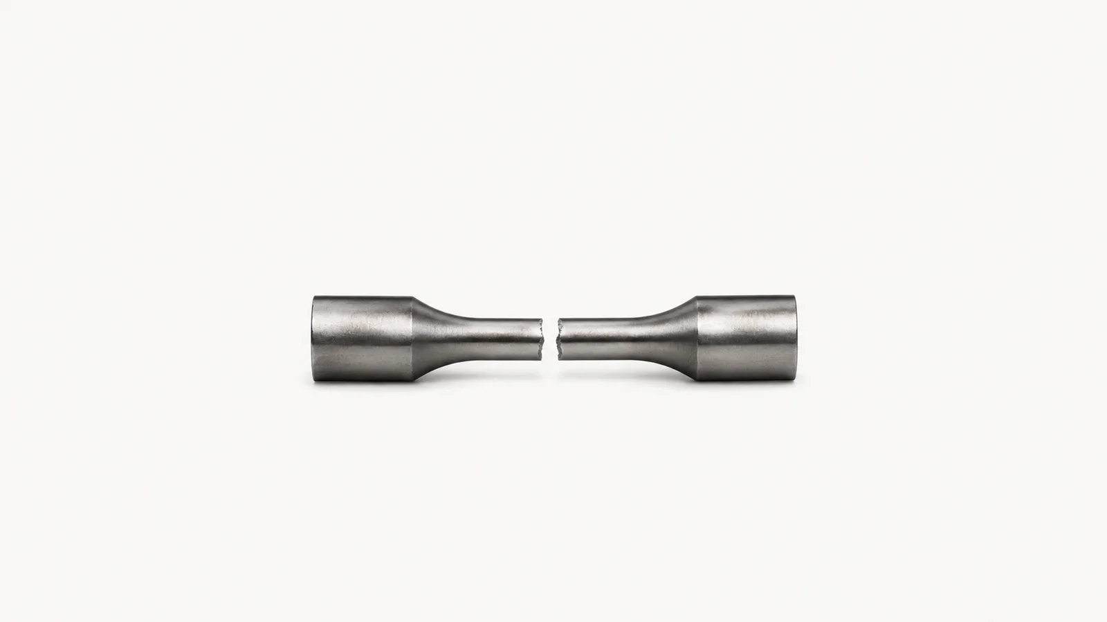 Isolated a machined steel test coupon with a fractured neck centred on a seamless pale off-white studio background, generous empty margin on every side for overlaid branding