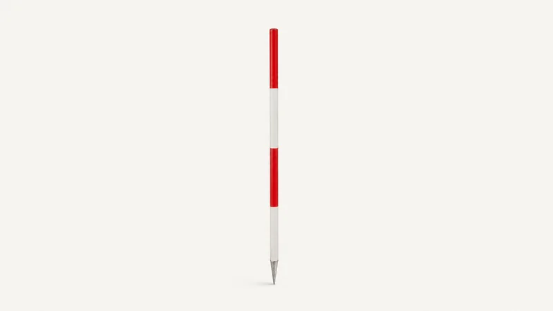 Isolated a red-and-white survey ranging pole with its steel point centred on a seamless pale off-white studio background, generous empty margin on every side for overlaid branding