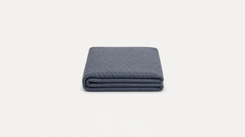 Isolated a padded quilted furniture blanket folded in a neat square centred on a seamless pale off-white studio background, generous empty margin on every side for overlaid branding