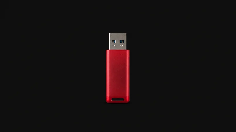 Isolated a USB boot drive with a red anodised shell centred on a seamless deep charcoal near-black studio background, generous empty margin on every side for overlaid branding