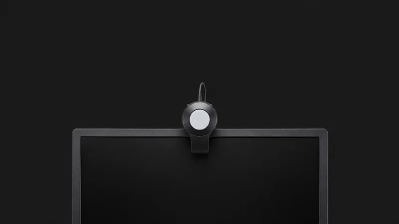 Isolated a colour-calibration puck resting on a monitor edge centred on a seamless deep charcoal near-black studio background, generous empty margin on every side for overlaid branding