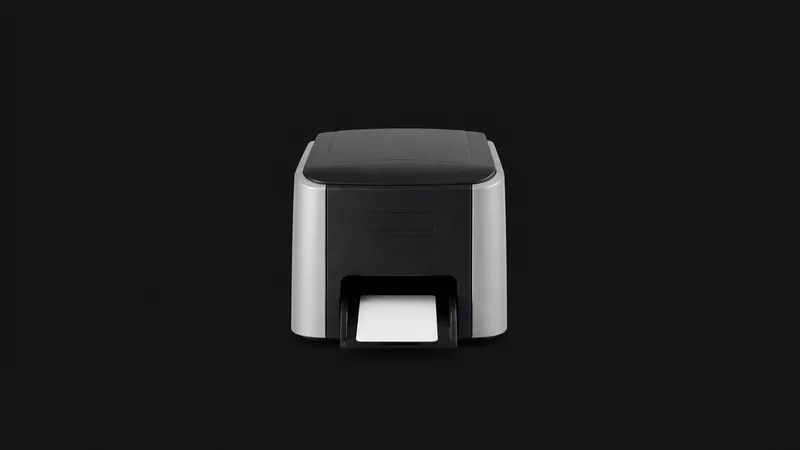 Isolated a desktop id-card printer with a blank card in its output tray centred on a seamless deep charcoal near-black studio background, generous empty margin on every side for overlaid branding