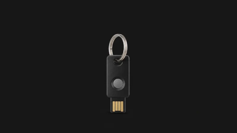 Isolated a hardware security key on a short steel keyring centred on a seamless deep charcoal near-black studio background, generous empty margin on every side for overlaid branding