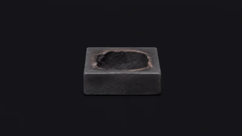 Isolated a graphite shaping block with a scorched hollow centred on a seamless deep charcoal near-black studio background, generous empty margin on every side for overlaid branding