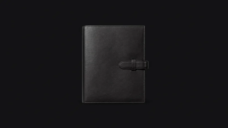 Isolated a leather-bound share certificate portfolio with a strap centred on a seamless deep charcoal near-black studio background, generous empty margin on every side for overlaid branding