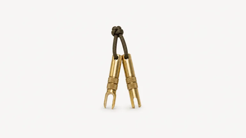 Isolated a set of brass keycap pullers on a cord centred on a seamless pale off-white studio background, generous empty margin on every side for overlaid branding