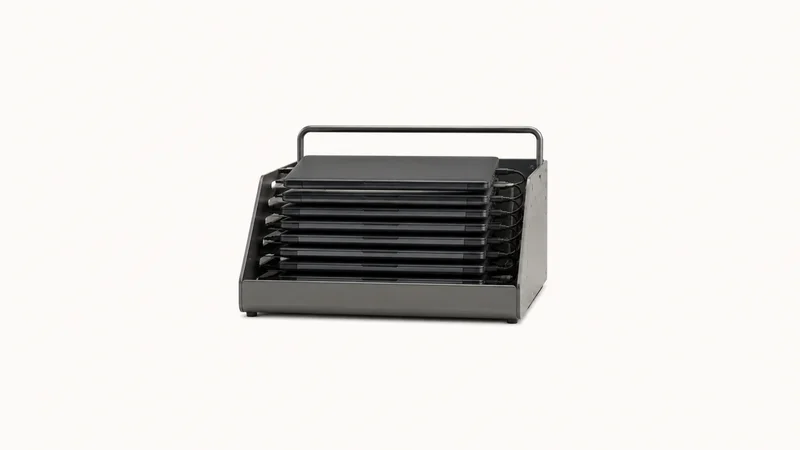 Isolated a charging cart tray of stacked student laptops with lids closed centred on a seamless pale off-white studio background, generous empty margin on every side for overlaid branding