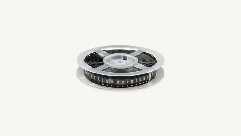 Isolated a reel of surface-mount capacitors on tape centred on a seamless pale off-white studio background, generous empty margin on every side for overlaid branding