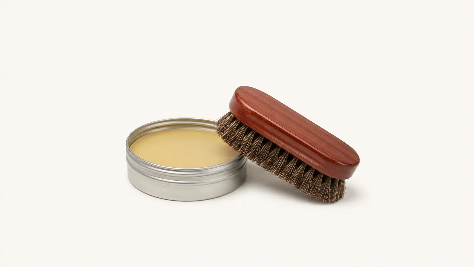 Isolated a tin of paste wax with a coloured horsehair polishing brush centred on a seamless pale off-white studio background, generous empty margin on every side for overlaid branding