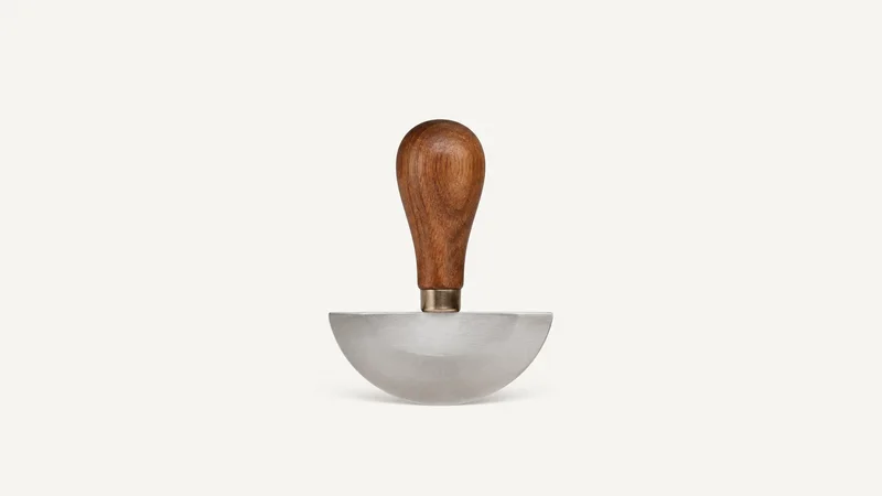 Isolated a head knife with a half-moon blade and a walnut handle centred on a seamless pale off-white studio background, generous empty margin on every side for overlaid branding
