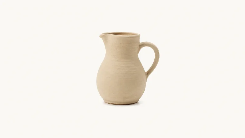 Isolated a bisque-fired jug awaiting glaze centred on a seamless pale off-white studio background, generous empty margin on every side for overlaid branding