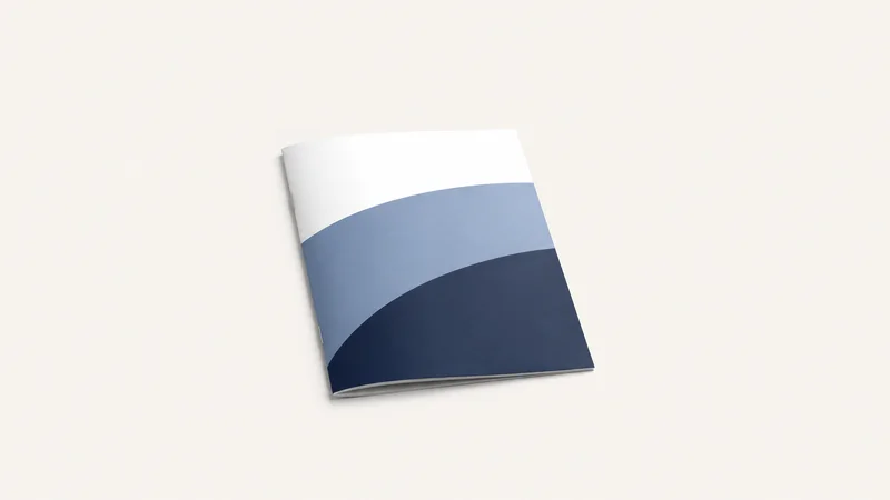 Isolated a saddle-stitched booklet with a folded cover centred on a seamless pale off-white studio background, generous empty margin on every side for overlaid branding