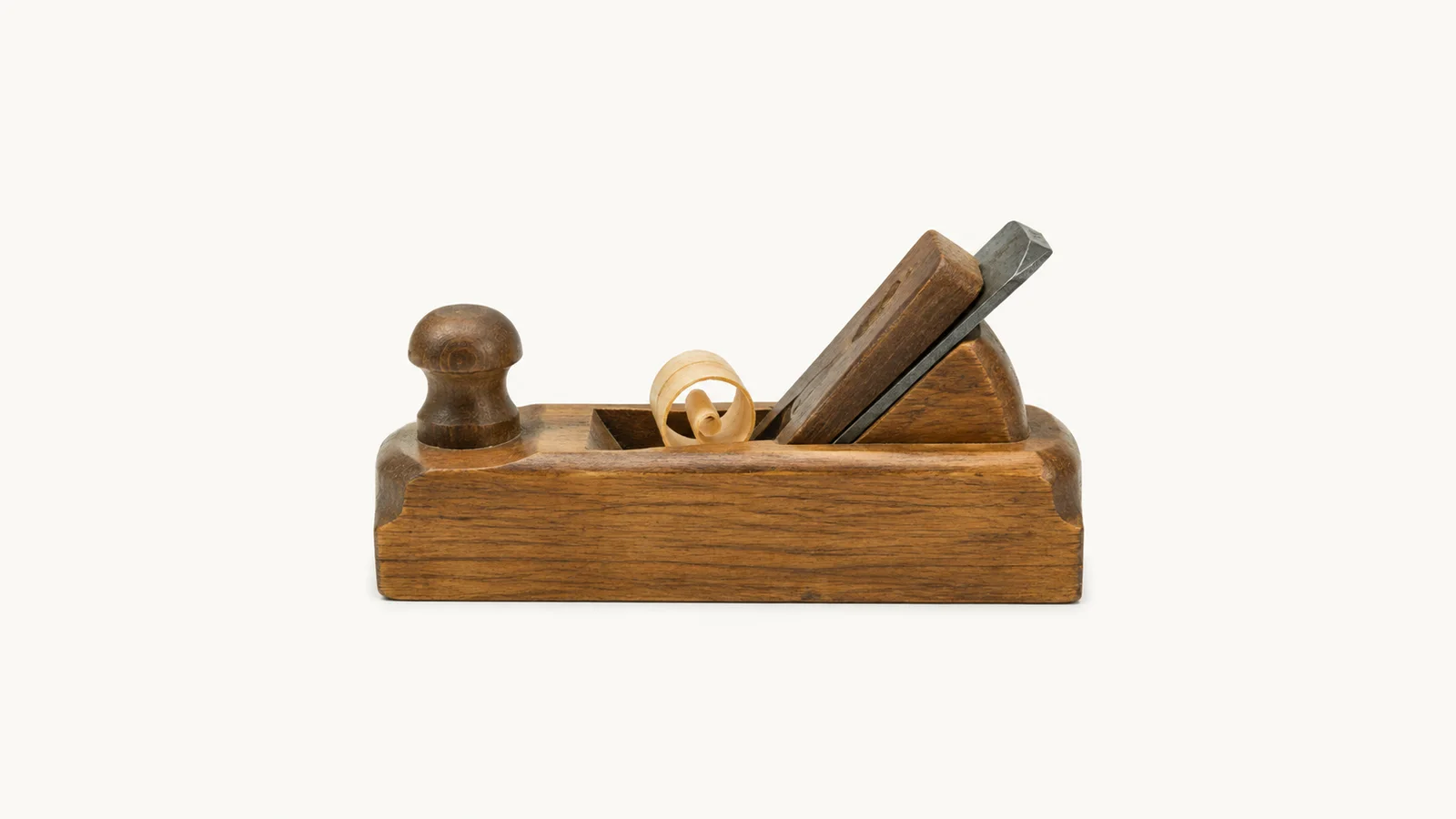 Isolated a wooden jack plane with a shaving curling from the mouth centred on a seamless pale off-white studio background, generous empty margin on every side for overlaid branding