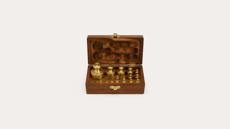 Isolated a set of brass balance weights in a wooden box centred on a seamless pale off-white studio background, generous empty margin on every side for overlaid branding