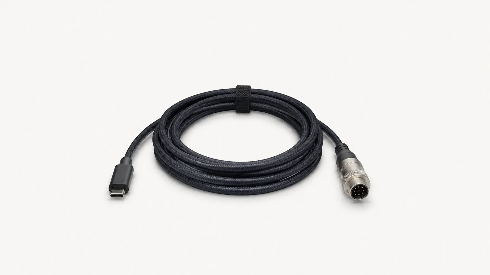 Isolated a coiled USB-C cable with an aviator connector centred on a seamless pale off-white studio background, generous empty margin on every side for overlaid branding