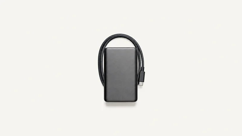 Isolated an external solid-state drive with a braided cable centred on a seamless pale off-white studio background, generous empty margin on every side for overlaid branding