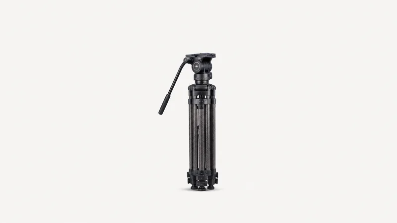 Isolated a fluid-head tripod with folded carbon legs centred on a seamless pale off-white studio background, generous empty margin on every side for overlaid branding