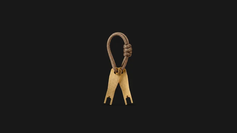 Isolated a set of brass keycap pullers on a cord centred on a seamless deep charcoal near-black studio background, generous empty margin on every side for overlaid branding