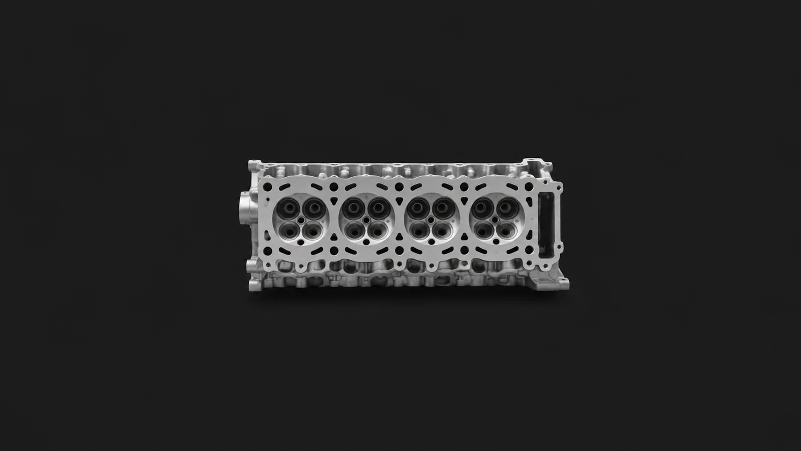 Isolated a bare car cylinder-head casting with valve seats centred on a seamless deep charcoal near-black studio background, generous empty margin on every side for overlaid branding